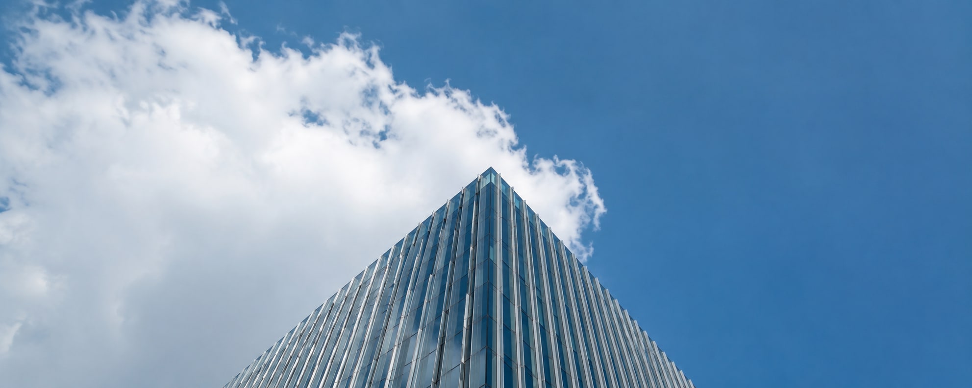 A glass office tower rising against a blue sky with clouds.